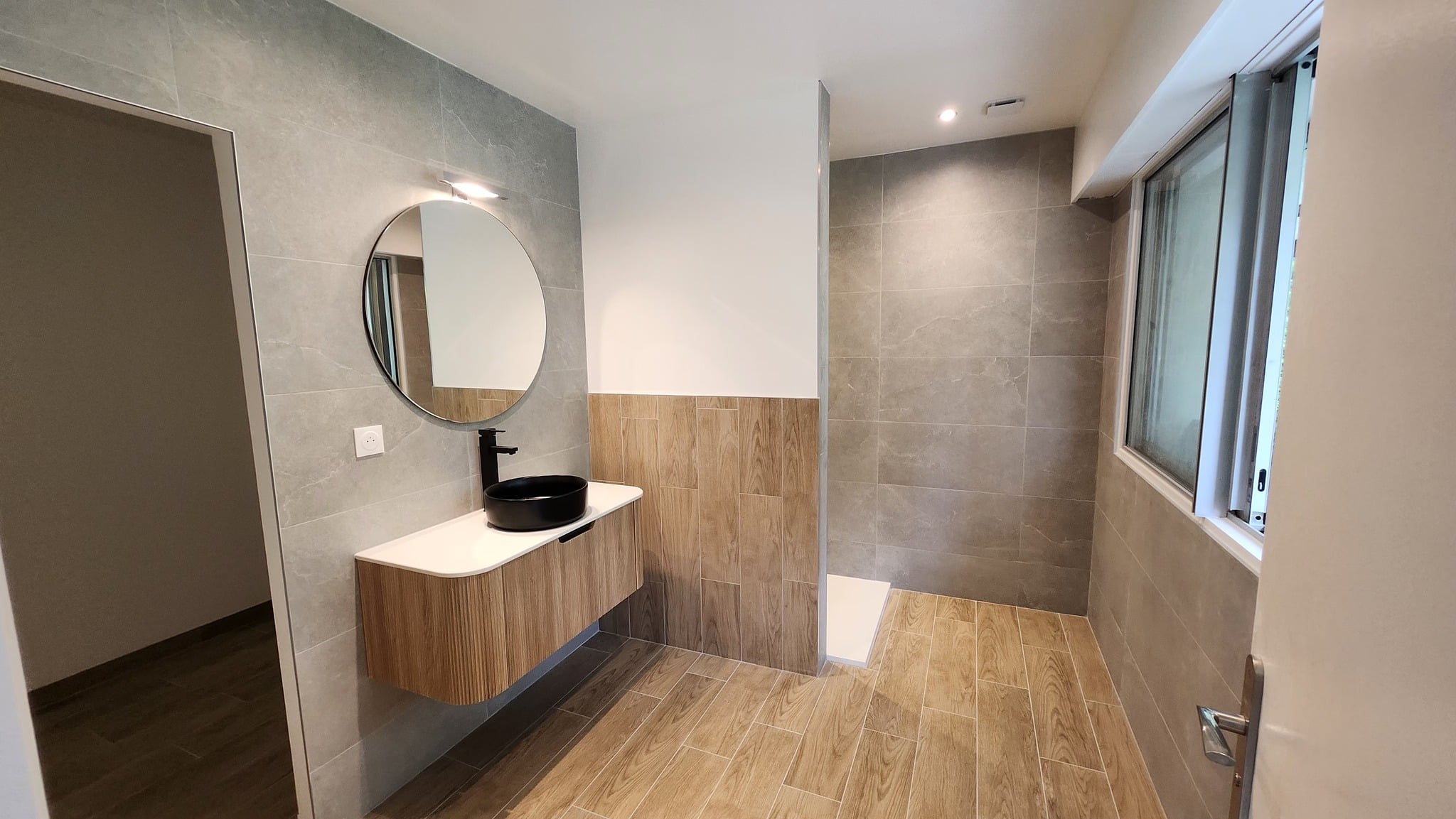 Salle de bains rénovée avec vasque suspendue, miroir rond et douche à l'italienne