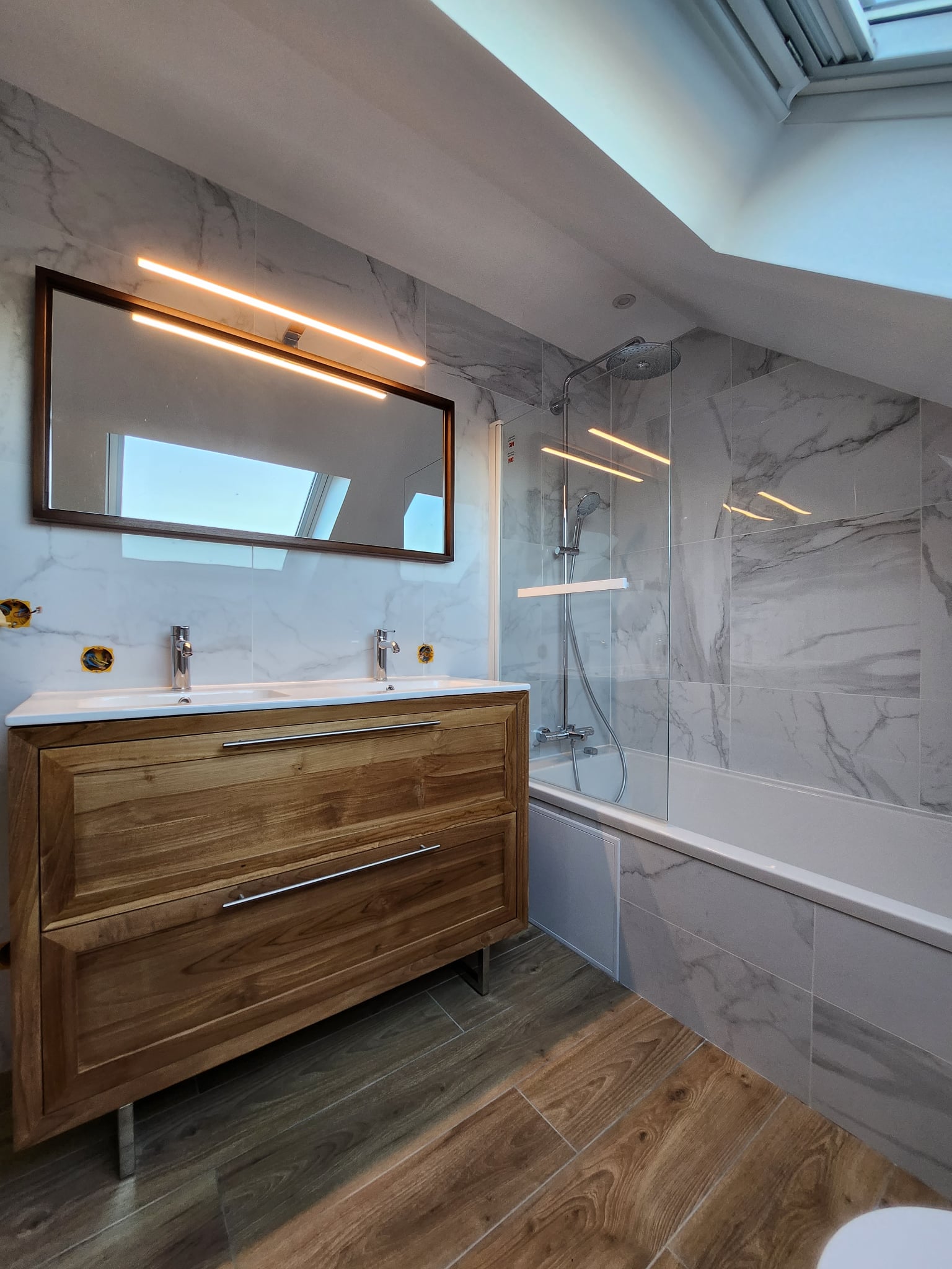 Salle de bains sous combles avec meuble double vasque en bois et faïence effet marbre